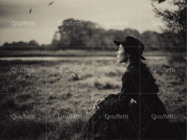 Sepia-toned, vintage-look portrait of a contemplative woman sitting in a meadow.